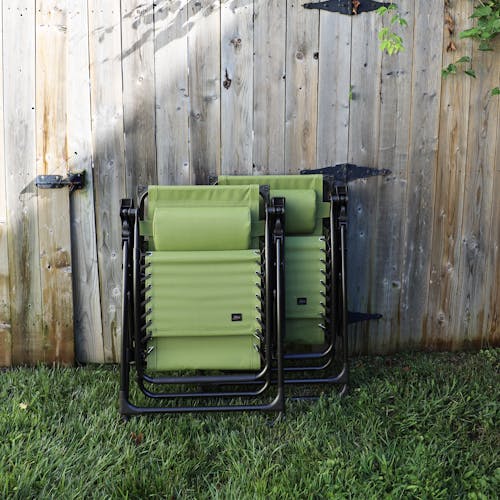 Set of 2 26-inch sage green gravity free chairs folded and leaning against a fence.