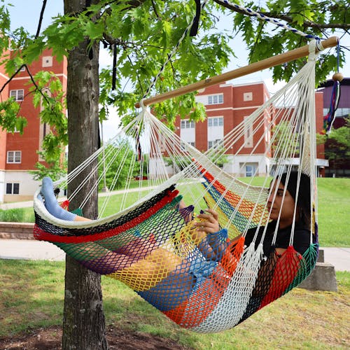 Girl relaxing in the Bliss Hammocks 40-inch Multi-Color Island Rope Hammock Chair hanging from a tree.