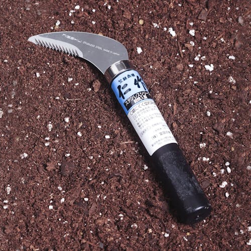 Nisaku Zassou Nukigama 2.75-inch Saw Tooth Sickle laying in soil.