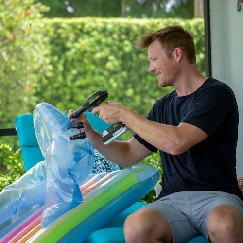 Man using the Sun Joe 24-Volt Cordless High-Volume Inflator with a 1.3-Ah battery attached to fill a pool tube.