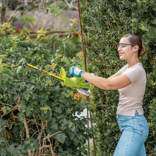 Woman using the Sun Joe 24-volt cordless 18-inch hedge trimmer to trim a bush.