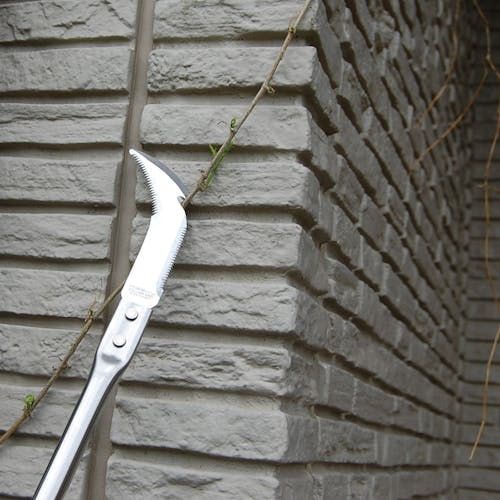 Nisaku 24-inch Scheve Cutter Japanese Stainless Steel Curved Cutter cutting a vine off a brick wall.