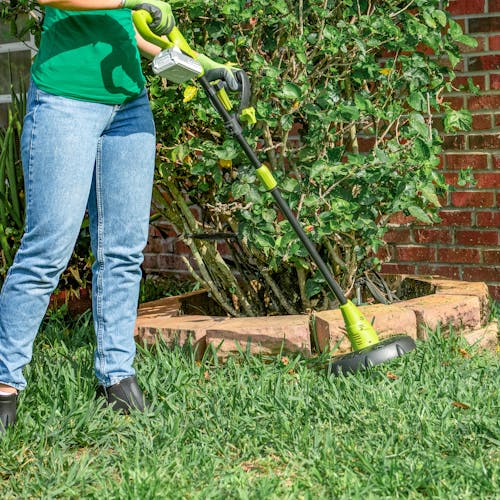 Person using the Sun Joe 24-volt cordless 10-inch stringless grass trimmer with a 2.0-Ah lithium-ion battery to trim a lawn.