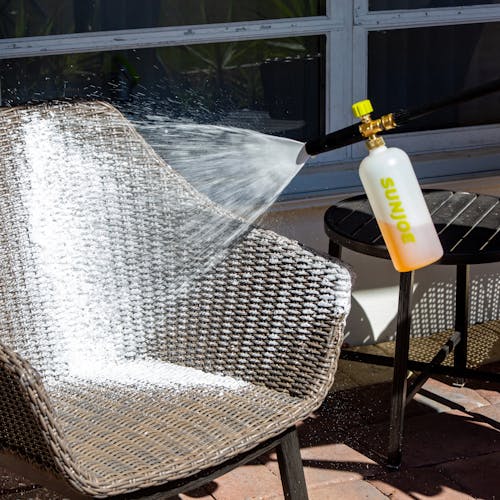 Sun Joe 34-ounce Foam Cannon for SPX Series Electric Pressure Washers spraying foam onto a patio chair.