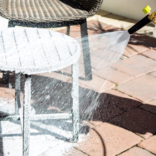 Sun Joe 34-ounce Foam Cannon for SPX Series Electric Pressure Washers spraying foam on a patio table.