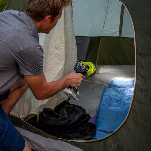 Man using the Sun Joe 24-Volt Cordless Flashlight/Flood Light/Spot Light to see the inside of his camping tent.