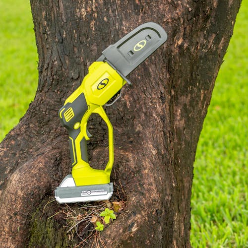 Sun Joe Cordless Handheld Chainsaw with its chain cover on, resting outside on a tree.