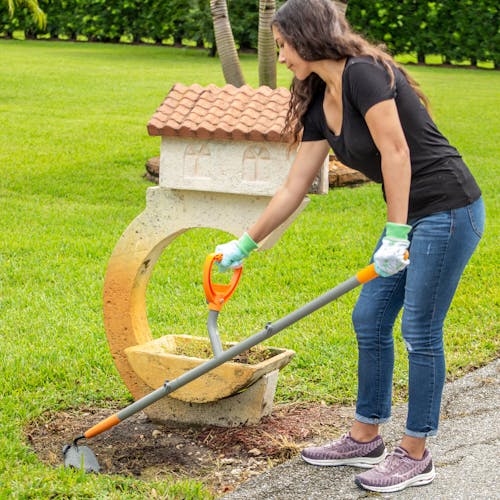 Woman using the ErgieSystems 54-inch Shank Pattern Garden Hoe with 6.25-inch blade to move dirt around a mailbox.