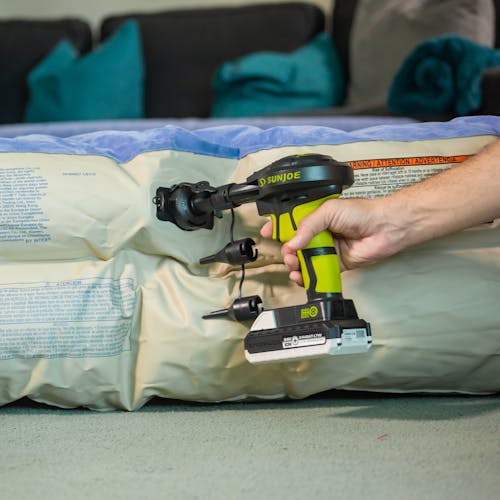 Person using the Sun Joe 24-Volt Cordless High-Volume Inflator with a 1.3-Ah battery attached to inflate an air mattress.