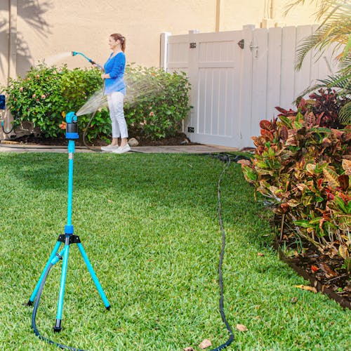 Aqua Joe Indestructible Turbo Drive 360 Degree Telescoping Tripod Lawn and Garden Sprinkler and Mister watering a lawn while a women waters a bush with an Aqua Joe hose and nozzle.