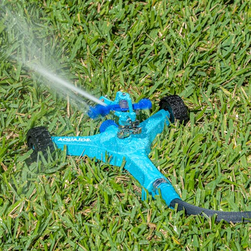 Aqua Joe 6-inch wheeled base Indestructible Zinc Impulse 360 Degree Sprinkler watering a lawn.