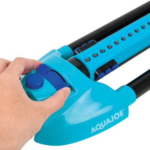 Person adjusting the range sliding tab on the Aqua Joe 20-nozzle Indestructible Metal Base Oscillating Sprinkler.