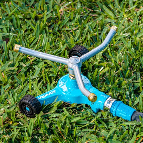 Aqua Joe Indestructible 3-Arm Zinc Rotary 360 Degree Sprinkler with wheeled base sitting in grass.