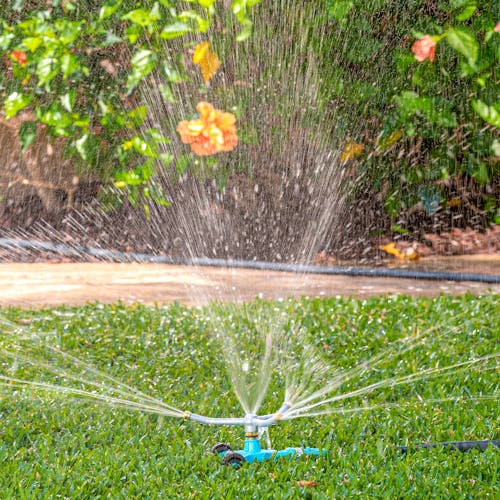 Aqua Joe Indestructible 3-Arm Zinc Rotary 360 Degree Sprinkler with wheeled base watering a lawn.