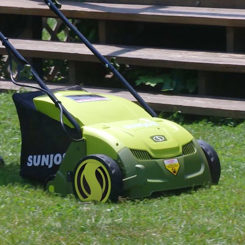 Sun Joe 12-amp 13-inch Electric Lawn Dethatcher with Collection Bag on a lawn.