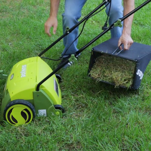 Person removing the collection bag on the Sun Joe 12-amp 13-inch Electric Lawn Dethatcher filled with grass.