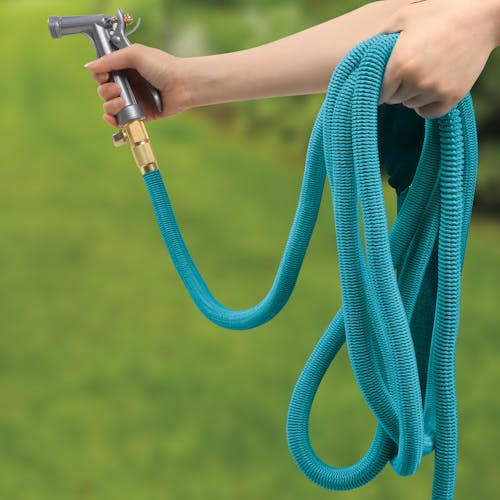 Person using the Aqua Joe 50-foot light blue No-Kink Expandable Garden Hose with a hose nozzle.