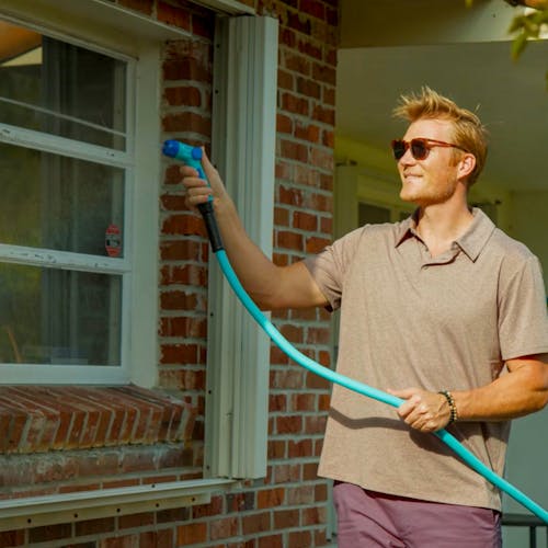 Man spraying side of home with Aqua Joe Hybridflex hose