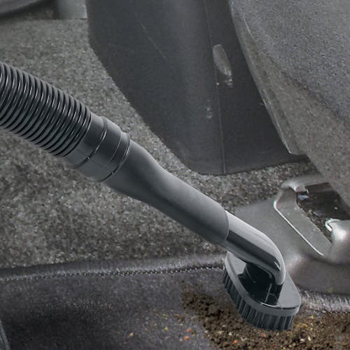 Auto Joe 12-Volt Portable Car Vacuum Cleaner with the extension hose and brush attachment being used to suck dirt off of a car floor.