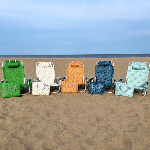 5 Backpack Aluminum Beach Chairs with different colors and patterns in a line on a beach with their matching cooler bags.