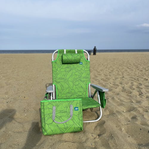Green banana leaves backpack beach chair on the sand with its matching cooler bag.