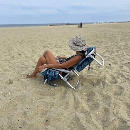 Woman relaxing on the beach in the Backpack Aluminum Blue Flower Beach Chair.
