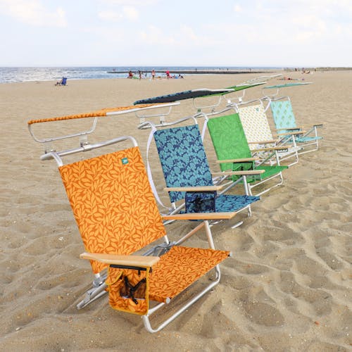 Angled view of 5 folding beach chairs with canopies on the beach, each with a different color and pattern.