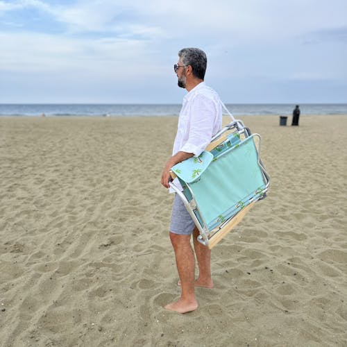 Man carrying the folding palm tree beach chair on his shoulder with the strap.