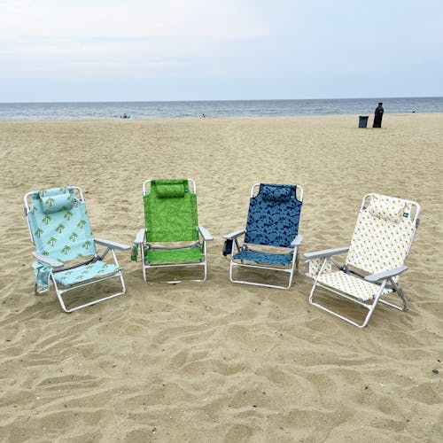 4 folding beach chairs on the sand, each with a different color and pattern.