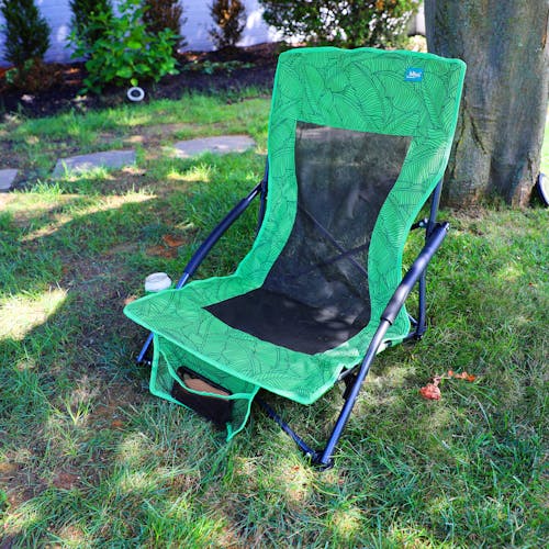 Collapsible green banana leaves beach chair on a lawn with a cellphone in the front pocket.