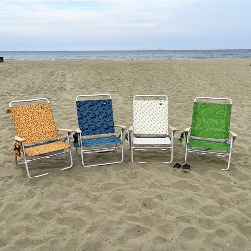 4 foldable beach chairs on the sand, each with a different color and pattern.