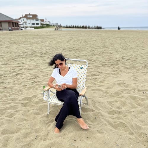 Woman on the beach looking at her phone while sitting in the foldable pineapple beach chair.