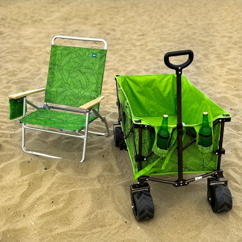 Foldable green banana leaves beach chair on the sand next to a matching beach cart.
