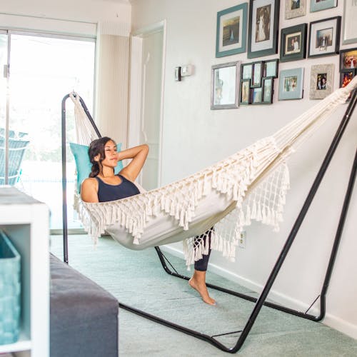 Woman laying in the Bliss Hammocks 40" Wide Hammock in a Bag with Fringe hung from a hammock stand indoors.