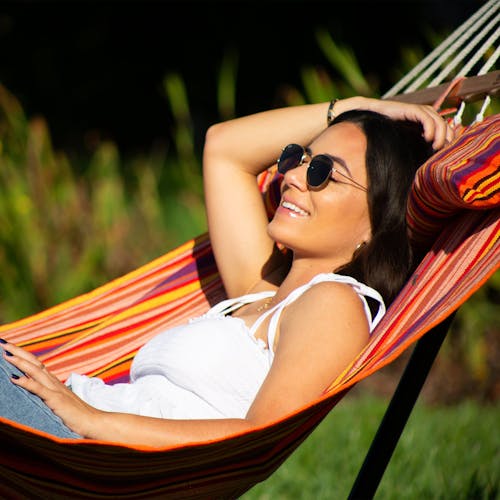 Woman relaxing outside in the sun in the Bliss Hammocks 48-inch Wide Toasted Almond Caribbean Hammock.