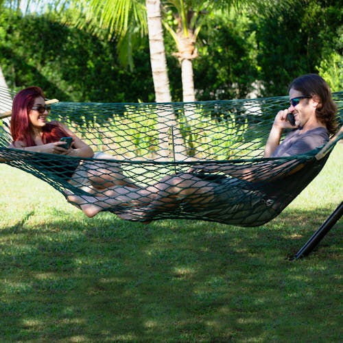 2 people laying across from each other in the Bliss Hammocks 60-inch Wide Green Cotton Rope Hammock.