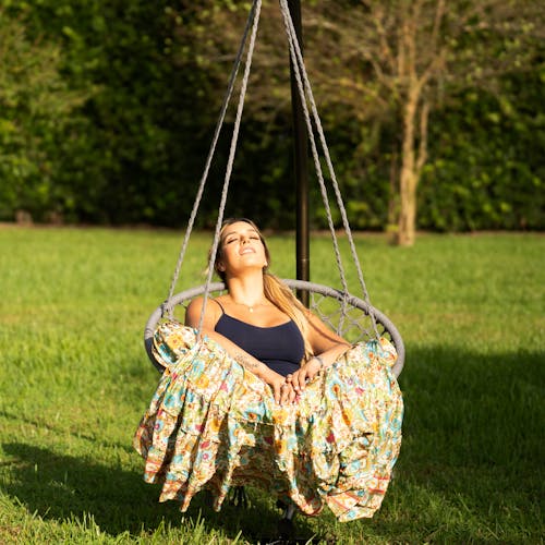 Woman sitting in the sun in the Bliss Hammocks 31.5-inch Wide Gray Macramé Swing Chair.