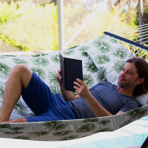 Man reading a book while laying in the 55-inch Green Burst Quilted Hammock.
