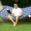 Man reading a book while sitting on the Bliss Hammocks 55-inch Blue Flowers Quilted Hammock.