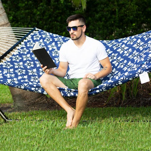 Man reading a book while sitting on the Bliss Hammocks 55-inch Blue Flowers Quilted Hammock.