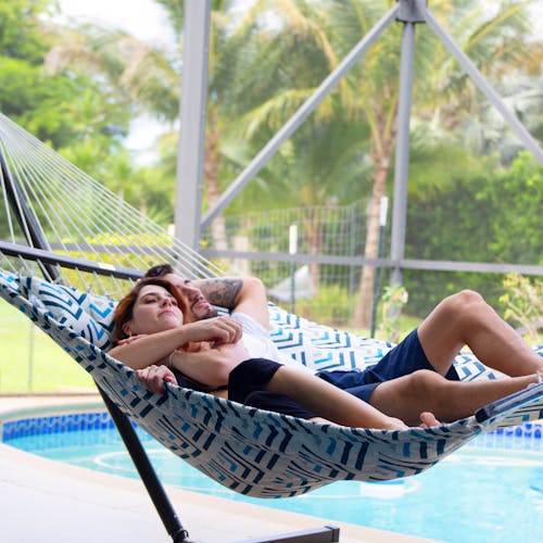 Couple laying in the Bliss Hammocks 55-inch Blue Geo Diamond Quilted Hammock next to a pool.