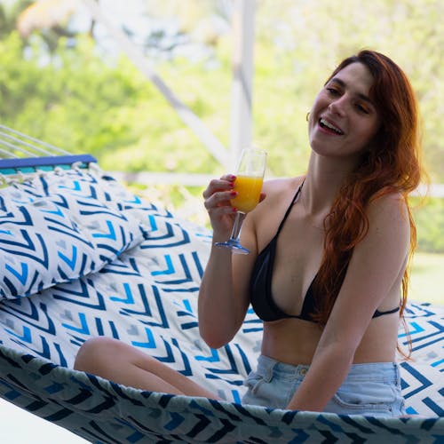 Woman sitting in the Bliss Hammocks 55-inch Blue Geo Diamond Quilted Hammock with a drink in her hand.