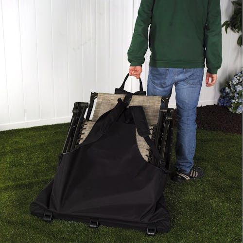 Person wheeling the gravity chair carrying bag across a lawn with a chair inside.