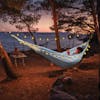 Person laying in a hammock at sunset with the strong lights hung around their hammock.