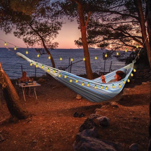 Person laying in a hammock at sunset with the strong lights hung around their hammock.