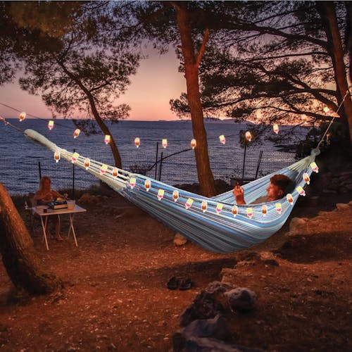 Person in a hammock at sunset with the string lights hung around them.