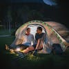 Couple sitting in the entrance to their tent at night with the string lights hung on the tent arch.