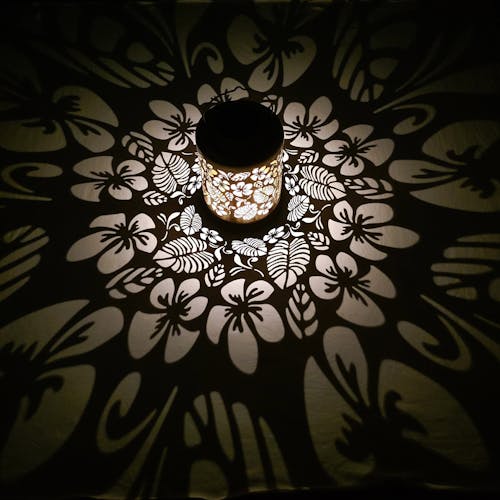 Lantern with tropical flower design creating a pattern of white light on the surface around it.