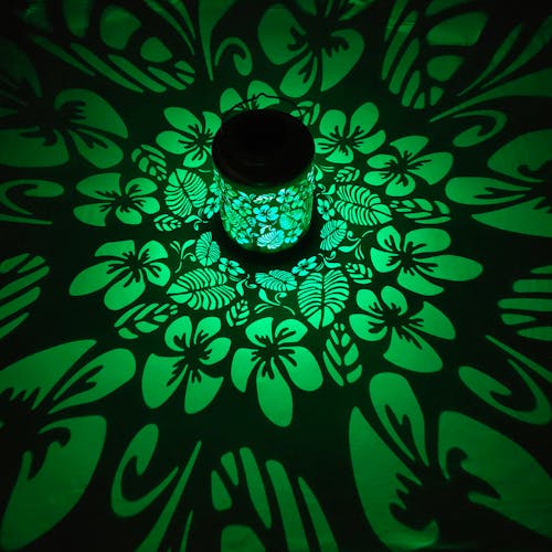 Lantern with tropical flower design creating a pattern of green light on the surface around it.