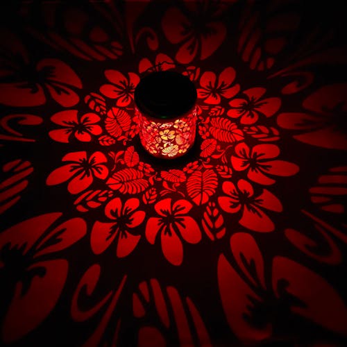 Lantern with tropical flower design creating a pattern of red light on the surface around it.